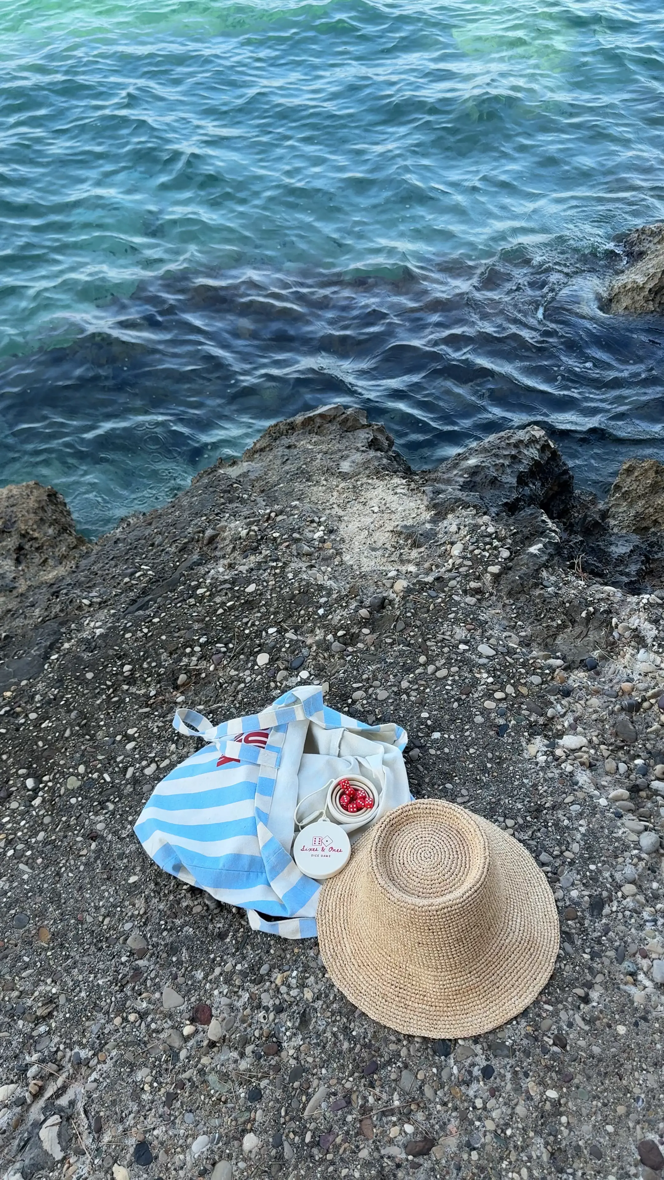 Turquoise water beside a rocky shore with a striped tote bag and straw hat